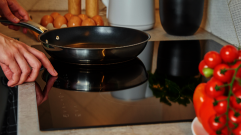 Afbeelding van iemand die een koekepan op een keramische kookplaat zet.