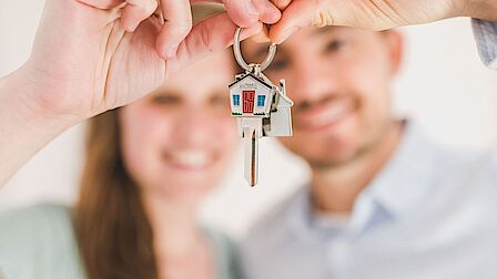 Een jong stel - vrouw en man - houden lachend een sleutel omhoog met een sleutelhanger van een huisje eraan